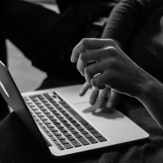 A black and white photo of a close up shot of a man's laptop being used.